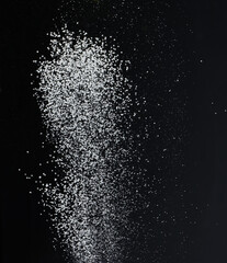 Obraz premium Close-up of white granular particles sugar, falling against a black background. High contrast and detailed texture of the grains