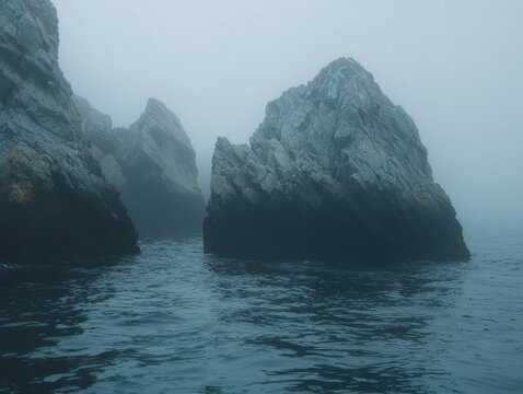 Misty ocean scene featuring striking rock formations emerging from the dark waters, shrouded in thick fog creating an eerie atmosphere.