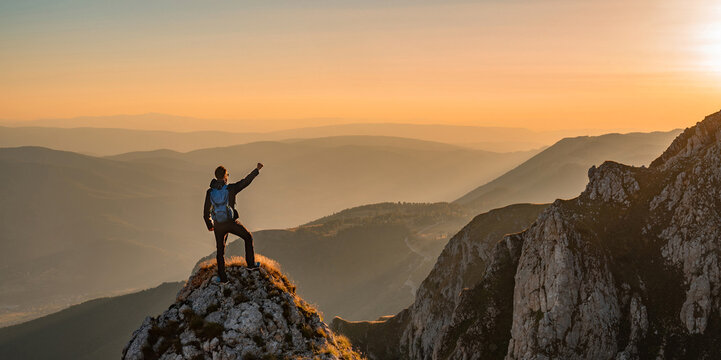 A happy man hikers standing with arms up on the mountain top celebrates successful completed hiking route with a panorama landscape, adventure travel. Concept of success, win, reaching a goals.