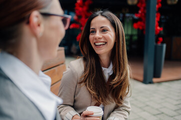 Two businesswomen having a coffee break and talking on a bench outside