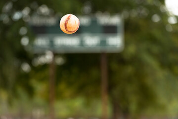 Little league baseball ball flying midair with scoreboard in background