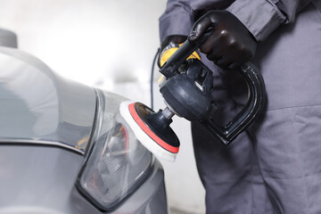 Man polishing car headlight with orbital polisher indoors, closeup