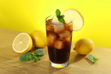 Refreshing iced cola with mint and lemons on wooden table
