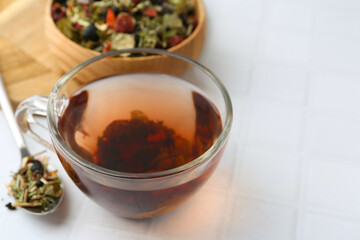 Delicious herbal tea and dry leaves on white tiled table, closeup. Space for text