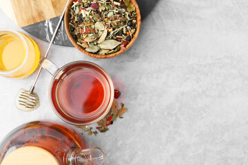 Delicious herbal tea with honey and dry leaves on grey table, flat lay. Space for text