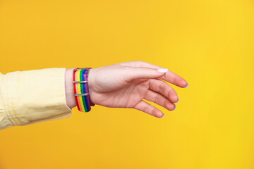 Woman wearing wristband in LGBT colors on orange background, closeup