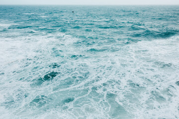 A vast expanse of ocean with turbulent waves and white sea foam. The deep blue water creates a...