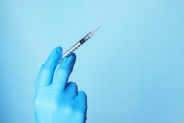 Doctor holding syringe with medication on dusty light blue background, closeup. Space for text