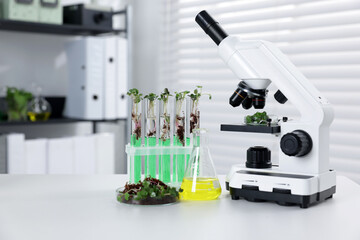 Biochemistry. Microscope, glassware with liquids and plants on white table in laboratory