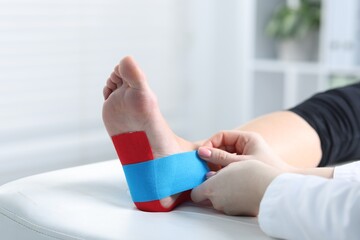 Doctor applying kinesio tapes to patient's foot in hospital, closeup