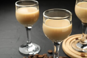 Coffee cream liqueur in glasses and beans on black table, closeup