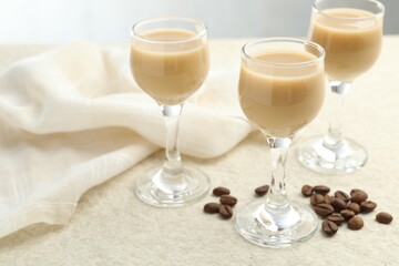 Coffee cream liqueur in glasses and beans on white textured table, closeup. Space for text