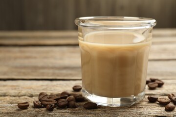 Coffee cream liqueur in glass and beans on wooden table, closeup. Space for text