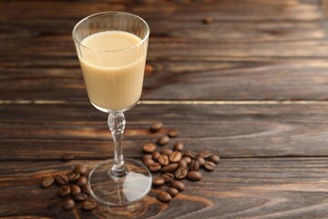 Coffee cream liqueur in glass and beans on wooden table, closeup. Space for text