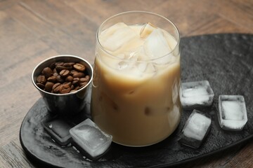 Coffee cream liqueur in glass, ice cubes and beans on wooden table, closeup