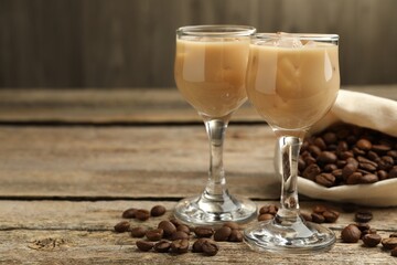 Coffee cream liqueur in glasses and beans on wooden table, closeup. Space for text
