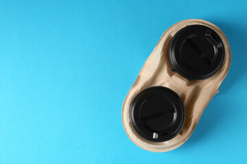 Paper coffee cups in cardboard holder on light blue background, top view. Space for text
