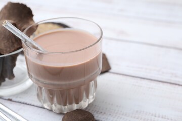 Tasty chocolate milk in glass and pieces of chocolate on white wooden table, closeup. Space for text