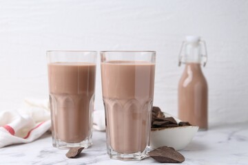 Tasty chocolate milk in glasses and pieces of chocolate on white marble table