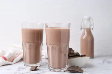 Fototapeten Tasty chocolate milk in glasses and pieces of chocolate on white marble table © New Africa