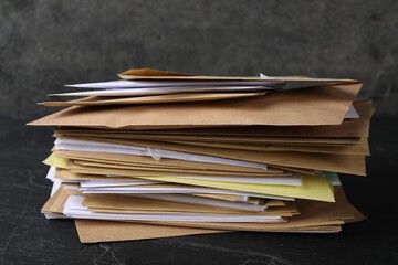 Stack of different paper envelopes on black table, closeup. Post office