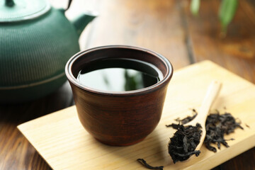Freshly brewed tea in cup and dried leaves on table, closeup