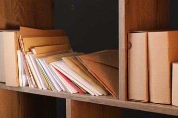 Different paper envelopes and parcels on wooden shelves in post office, closeup