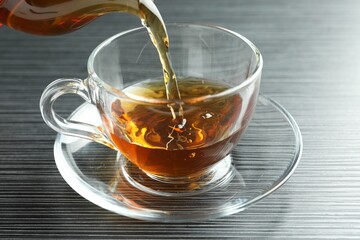Pouring aromatic tea into cup at black wooden table, closeup