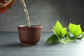 Pouring aromatic tea into cup at black wooden table against grey background, closeup