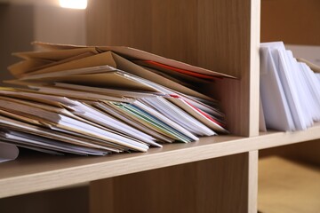 Different paper envelopes on wooden shelves in post office, closeup