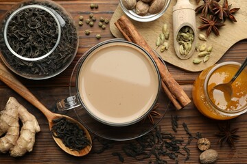 Aromatic Masala tea in cup, spices, dry leaves and honey on wooden table, flat lay