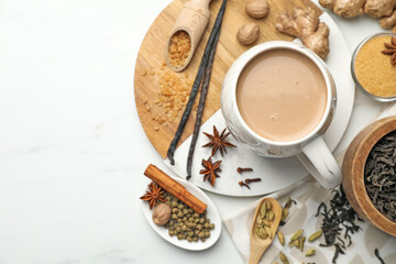 Aromatic Masala tea in cup, brown sugar, dry leaves and spices on white marble table, flat lay