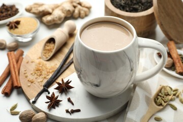 Aromatic Masala tea in cup, brown sugar and spices on white table, closeup