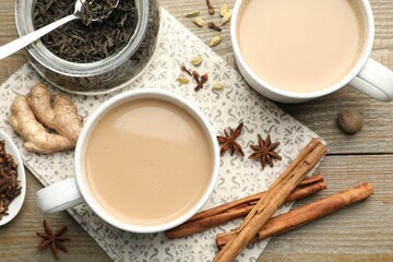 Aromatic Masala tea in cups, dry leaves and spices on wooden table, flat lay