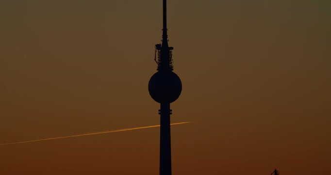 Silhouette von Fernsehturm in Berlin mit Flugzeug in Hintergrund.
