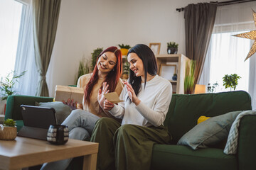 two women sisters or friends open presents in front of digital tablet