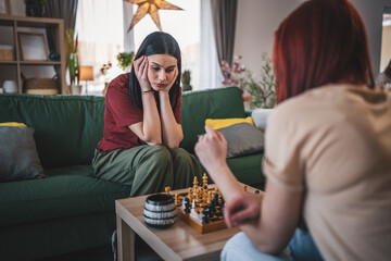 two women young females sisters friends play chess board game at home