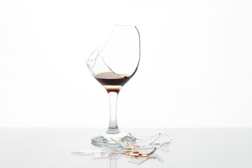Pieces of broken glass with wine on table against white background