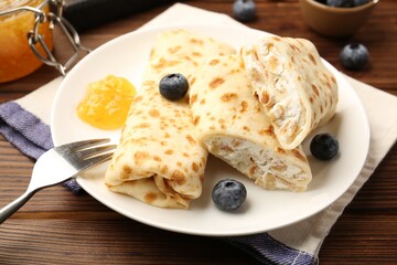Delicious crepes with cottage cheese, jam and blueberries served on wooden table, closeup