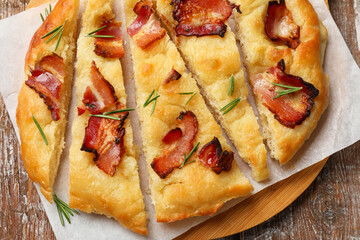 Slices of delicious focaccia bread with bacon and rosemary on wooden table, top view