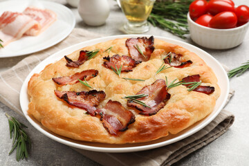Delicious focaccia bread with bacon, rosemary, oil and tomatoes on light grey table, closeup