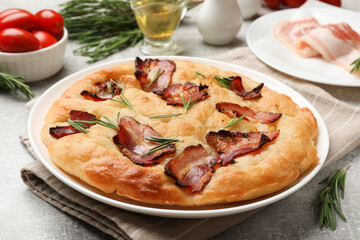 Delicious focaccia bread with bacon, rosemary, oil and tomatoes on light grey table, closeup