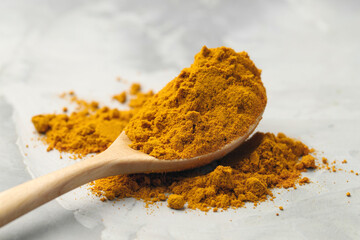 Turmeric powder and spoon on light grey table, closeup