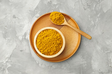 Turmeric powder in bowl and spoon on light grey table, top view