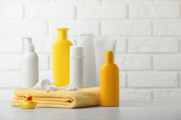 Baby cosmetic products, towel and rubber duck on table against white brick wall. Space for text