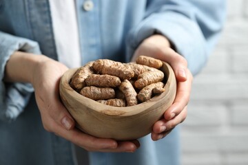 Woman holding bowl with raw turmeric roots on light background, closeup