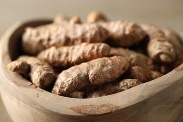 Raw turmeric roots in wooden bowl, closeup