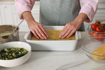 Woman making spinach lasagna at marble table indoors, closeup