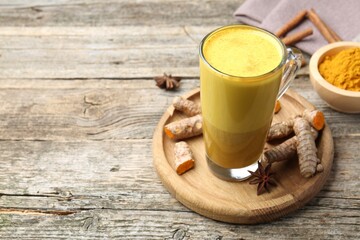Delicious turmeric latte in glass cup, roots and spices on wooden table. Space for text