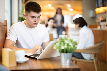 Young man working on laptop drinking coffee in cafe